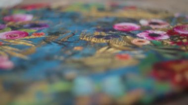 Ahşap masanın üzerinde çiçek desenli bir çizim olan renkli bir el yapımı minderin kapağı. Yavaş çekim, yüzeysel alan derinliği. 