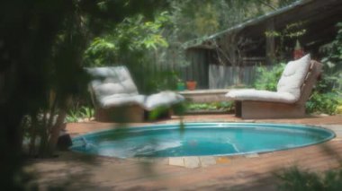 Küçük bir havuzun yanında yumuşak beyaz yastıklı iki sandalye. Yavaş çekim, yüzeysel alan derinliği. 