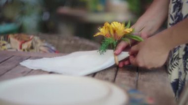 Kadın, yemek masasını hazırlamak için peçeteye çiçek düzenliyor. Yavaş çekim, yüzeysel alan derinliği.