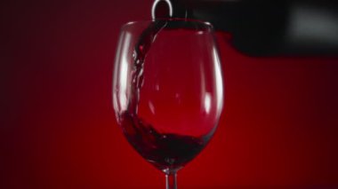 Red wine pouring into a glass from the battle on a red background. Slow motion. 