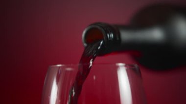 Close up of a bottle pouring red wine into a wineglass on a red background. Slow motion. 