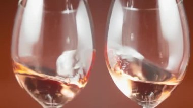 Two glasses of rose wine rotating against the amber background. Slow motion. 