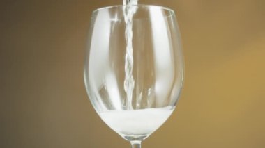 Close up of pouring sparkling white wine on a golden background. Slow motion.