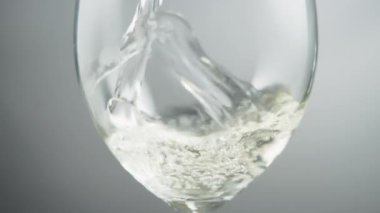 Close up of white wine swirling in a wineglass on a grey background. Slow motion.