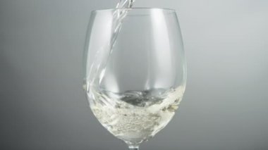 Close up of pouring white wine in a wineglass on a grey background. Slow motion.