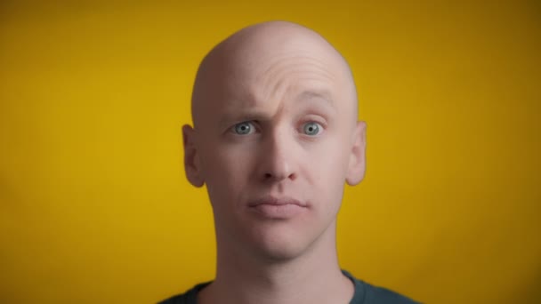 青い目と明るい肌を持つ男がカメラに向かってまっすぐ見て 黄色の背景に1つの眉を上げる リアルタイム — ストック動画