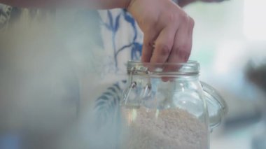 Kadın şef elleriyle cam kavanozdan pirinç alıyor. Yavaş çekim, yüzeysel alan derinliği. 