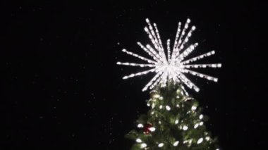 Bir Noel ağacının tepesinde gece yağan karla aydınlatılmış yıldız süslemesi. Yavaş çekim. 