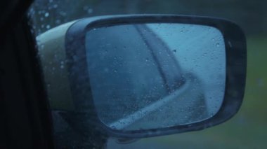 Yolculuk sırasında yağmur damlalarıyla kaplı bir arabanın dikiz aynası. Ağır çekim, yakın çekim..