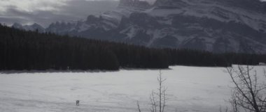 Kışın Kanada Kayalıkları 'nda donmuş gölden geçen iki kişi. Yavaş çekim. 