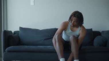 Genç adam evdeki kanepede otururken ayakkabılarını giyiyor. Sağlıklı yaşam tarzı ve spor. Yavaş çekim. 