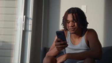 Dehşet saçan genç adam evde akıllı telefonunu kullanırken gülümsüyor. Yavaş çekim. 