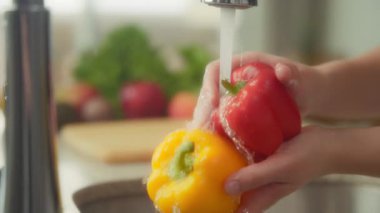 Mutfak lavabosunda kırmızı ve sarı dolmalık biberleri yıkayan kadına yaklaş. Yavaş çekim. 