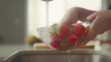 Çilekleri cam bir kasede musluk suyuyla yıkayan kadınların ellerini kapatın. Yavaş çekim. 