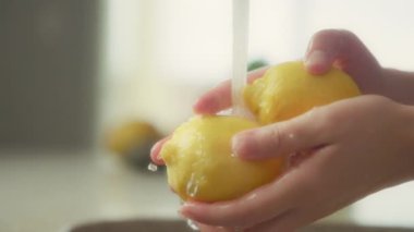 Musluk suyunun altında sarı limon yıkayan kadınların ellerini kapatın. Yavaş çekim.