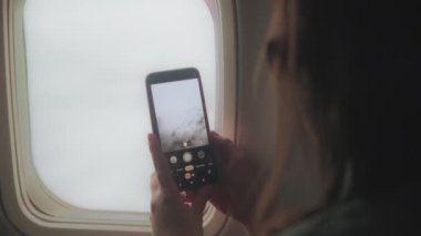 Bir kadın uçuş sırasında uçak penceresinden bulutların fotoğrafını çekiyor. Yavaş çekim.