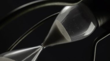 Siyah zemin üzerinde dönen eski kum saatinin soyut görüntüsü.