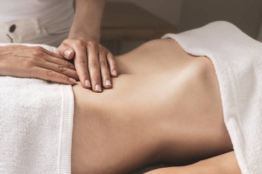 Bir kadın kaplıcada karnına masaj yaptırıyor, eklemlerine, ellerine, kollarına, bacaklarına, boynuna, beline, kalçalarına ve dizlerine odaklanıyor.