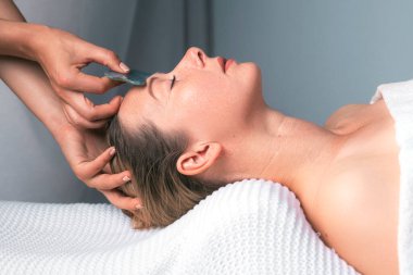 Bir kadın kaplıcada alnına masaj yaptırıyor, terapistlerin nazikçe vücudunda süzüldüğünü hissediyor. Çenesi gevşemeye başlar, boynunda ve kaslarında gerilim oluşur.