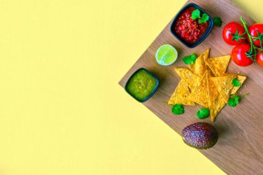Parlak sarı arkaplanda salsa sosu, guacamole ve doğranmış domates içeren canlı ve renkli bir nacho tabağı.