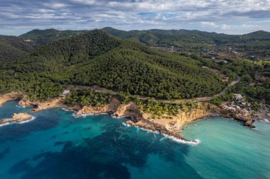 Güneşli bir yaz günü mavi gökyüzü ve turkuaz suyla birlikte İbiza adasındaki Cala Xarraca sahillerinin havadan çekilmiş fotoğrafları.