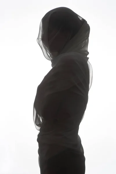 Silhouette of female body in profile fully wrapped in chiffon fabric on white background