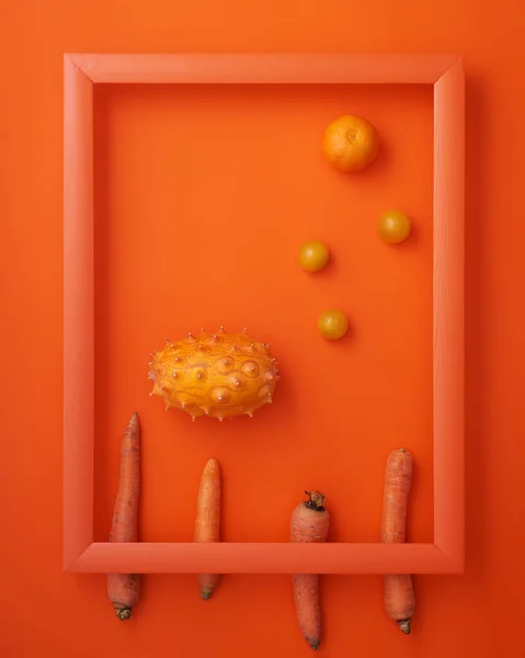 メロン チェリートマト クレメンタイン ニンジンをオレンジの背景に木製の画像フレームに入れました ストックフォト