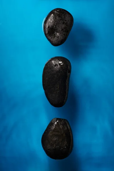 柔らかい波を持つ明るい青い海の水の中に3つの大きな滑らかな黒い石 ロイヤリティフリーのストック写真