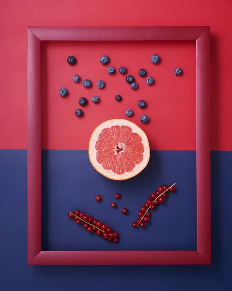 半分にカットグレープフルーツ 赤と青の背景に木製の画像フレームでブルーベリーとスグリ ストック画像