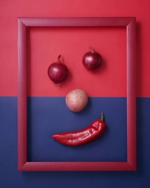赤と青の木枠の中で笑顔の顔の形をした玉ねぎ ジャガイモ コショウの背景 ストック画像