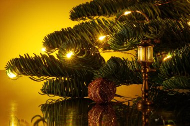 Clouse up of Christmas tree branch decorated with warm yellow lights, sparkly ornament and vintage copper flashlight clipart