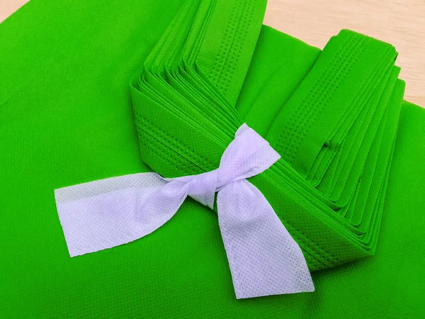 pile of green porous tote bags. non-woven fabric material tied with white rope. polypropiline bags on wooden planks
