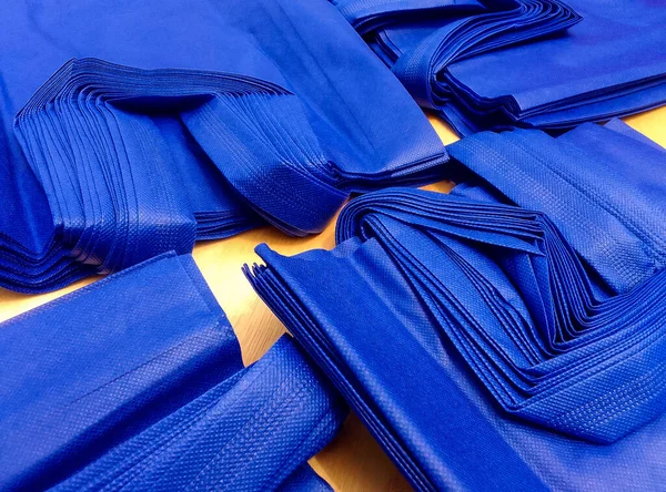 pile of dark blue non-woven fabric tote bags on brown wooden planks. collections made of non-woven fabrics. textured and porous polypropylene bags. partially sighted