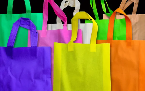 a bunch of colorful polypropylene tote bags on a black background. spunbond bag