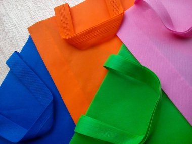 Pembe, yeşil, turuncu ve mavi polipropilen çantalar. Beyaz lifli bir tahtanın üzerinde kıvrımlı dokumasız kumaştan yapılmış bir çanta yığını.