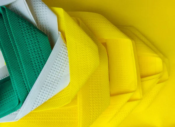 stock image non woven tote bag in green, yellow and white. a set of stacked and folded porous polypropylene tote bags