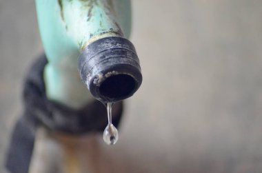 Mavi plastik bir musluktan temiz su damlacıkları. Kırık ve yosunlu bir musluktan yıkık dökük bir binanın arka planına düşmek.