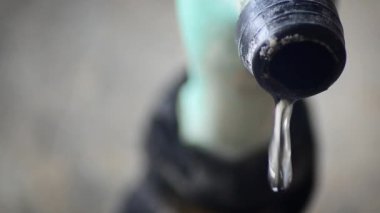 Mavi plastik bir musluktan temiz su damlacıkları. Kırık ve yosunlu bir musluktan yıkık dökük bir binanın arka planına düşmek.