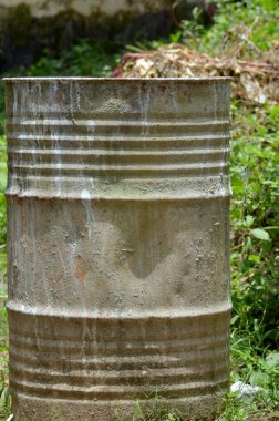 Bahçede yabani otlarla dolu eski ve kirli bir davul. büyük teneke kova