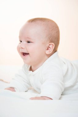 Sevimli, gülümseyen bebek yatakta yatıyor, turuncu arka plan.