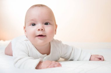 Battaniyenin üzerine uzanmış, turuncu arka planda gülümseyen şirin bebek.