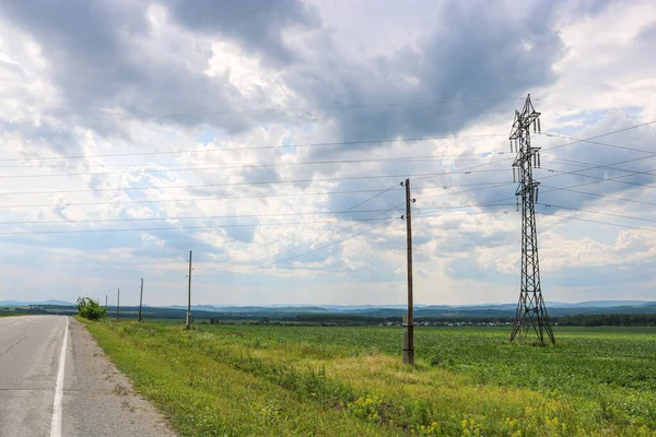 Power transmission towers over a rural field in the countryside. Gloomy sky with clouds.