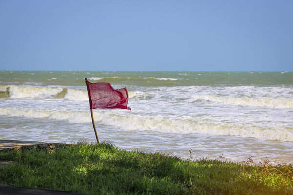 Red warning flag flapping in the wind on beach at stormy weather. Swimming is dangerous in sea waves.