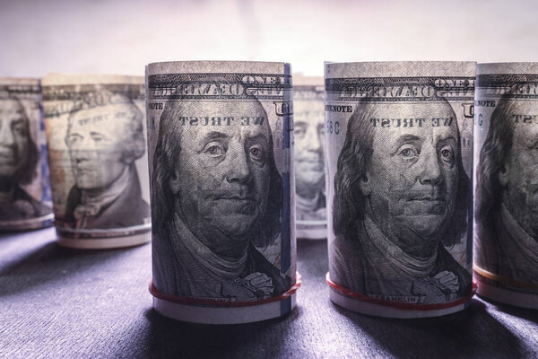 Долларовые купюры закатываются в рулоны в подсветке на темном фоне. Концепция финансов и экономики. Селективный фокус.