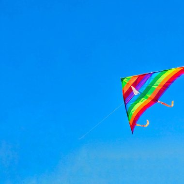 Rainbow kite flying in blue sky with clouds. Freedom and summer holiday concept. High quality photo