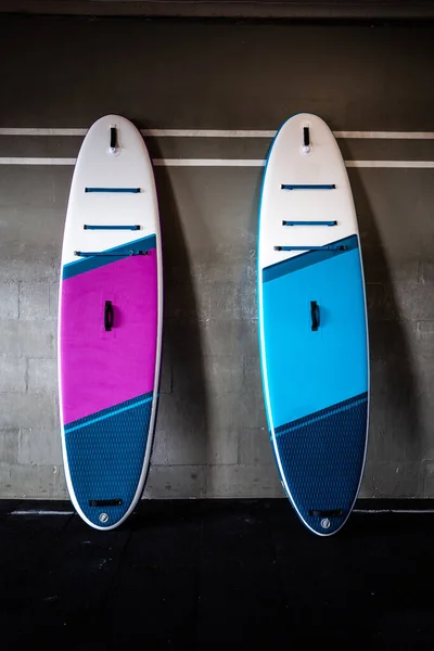 stock image Blue and pink stand-up paddle boards SUP by the wall. Surfing and sup boarding equipment close up.