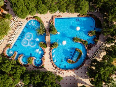 Lüks bir sahil otelinde geniş havuzlu ve slaytlı bir su parkı manzarası. Eğlenceli ve rahatlatıcı bir tatil için mükemmel..