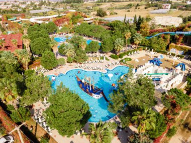 Lüks bir sahil otelinde geniş havuzlu ve slaytlı bir su parkı manzarası. Eğlenceli ve rahatlatıcı bir tatil için mükemmel..