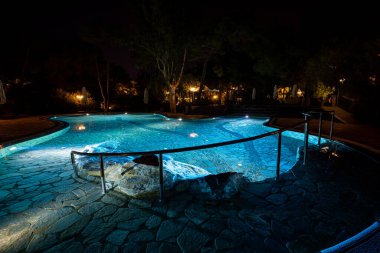 Lüks bir turistik otelde, güzel aydınlatılmış bir yüzme havuzuyla, geceleri yıldızların altında sakin bir ortam yaratarak rahatlayın.