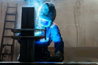 Fabrikada kaynak makinesiyle çalışan yetenekli bir metal işçisi güvenlik ekipmanı takıyor. El becerisi iş gücü kavramına göre metal imalatı ve inşaat bakım hizmeti